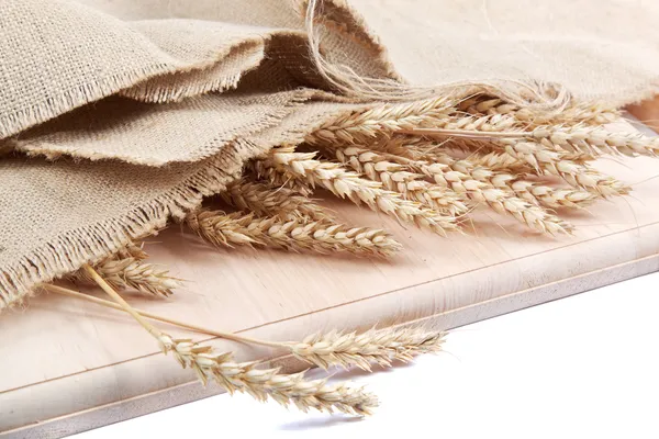 Ears of wheat under the canvas on a wooden board. — Stock Photo, Image