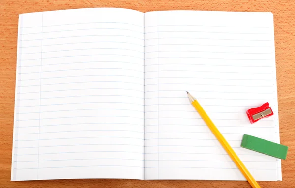 Um caderno aberto, lápis e artigos de papelaria em uma mesa de madeira . — Fotografia de Stock