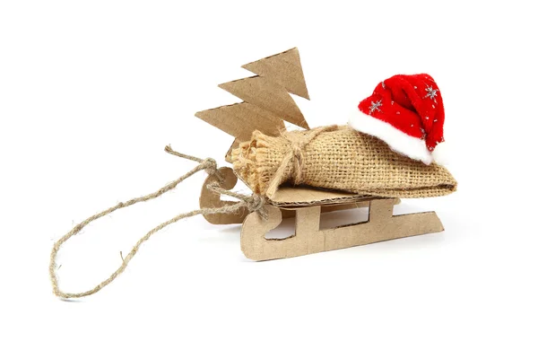 Sáně s pytloviny pytel, vánoční strom a santa claus klobouk. — Stock fotografie