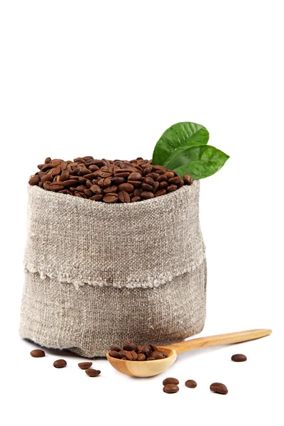 Café en grains dans un sac en toile, cuillère en bois et feuilles vertes . — Photo