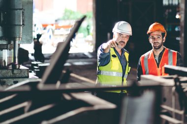 Güvenlik kasketli profesyonel teknisyenler endüstriyel fabrikada inşaat malzemelerinin bakımında çalışıyor. Üretim teknolojisinin imalat işiyle uğraşan denetçiler.