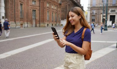 Güzel bir üniversite öğrencisi kadın. Şehirde yürüyor. Telefonda yazıyor.