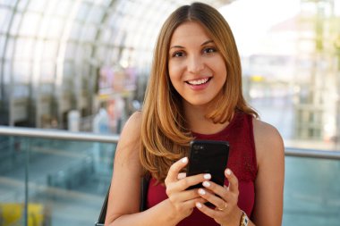Gülümseyen kız modern tren istasyonunda kameraya bakarak akıllı telefonu tutuyor. Mutlu kendine güvenen kadın, havaalanındaki mobil uygulamayla iptal ettiği uçuş için para iadesi alıyor. Yolcu hakları kavramı.