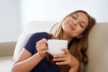 Rüya gibi gülümseyen pozitif kız gözleri kapalı sıcak bir içecekle bardağı tutarken kanepede oturduğumu hayal ediyorum.