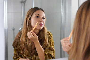 Yüz kılları alınıyor. Güzel genç bir kadın evde tıraş olurken yüzünü tıraş ediyor. Banyoda tıraş makinesi kullanan güzel bir kadın..