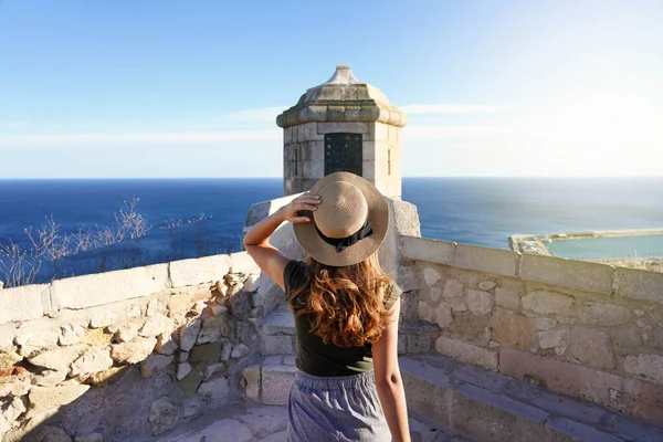 stock image Tourism in Alicante, Spain. Back view of traveler girl walking towards watchtower on Santa Barbara castle in Alicante city, Spain. Young female tourist visiting southern Europe.