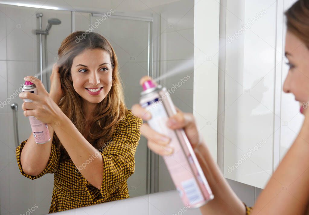 Fast and easy way to covering grey hair with instant spray dye. Young woman applying dry shampoo on her hair before going out.