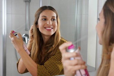 Güzel genç bir kadın dışarı çıkmadan önce saçına kuru şampuan sürüyor. Gri saçı sprey boyayla örtmenin hızlı ve kolay bir yolu..