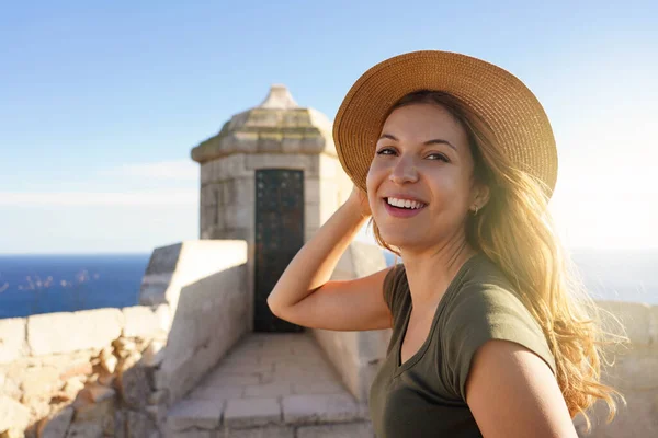 スペインのアリカンテにあるサンタバーバラ城にポーズをとって帽子をかぶった魅力的な若い女性のクローズアップ肖像画 リラックスした女の子を保持帽子と見てカメラ屋外 — ストック写真