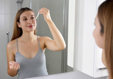 Genç Cilt Bakımı rutini. Güzel bir kız elinde pipeti tutarken yüzüne C vitamini antioksidan askorbik asit veriyor..