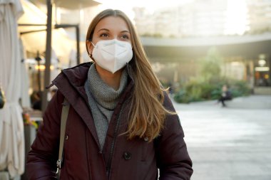 Şehrin arka planında tıbbi maske takan genç ve mutlu bir kadın.