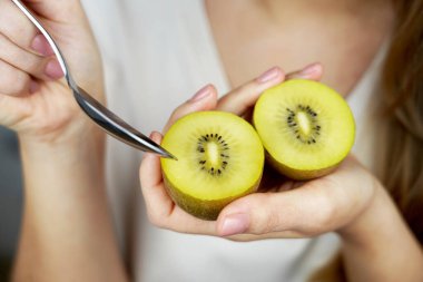 Elinde Kivi altın meyvesi var. Tatlı kaşığıyla olgun kivi yiyen bir kız. Sağlıklı beslenme ve C vitamini antioksidan konsepti için meyve.