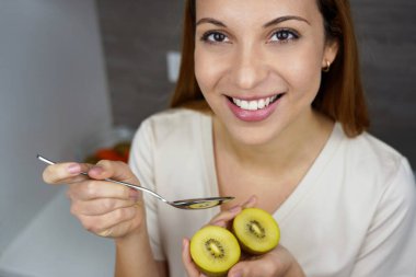 Evde gülümseyen ve altın kivi meyvesi yiyen güzel bir genç kadın. Yukarıdan yaklaş. Antioksidan, C vitamini, sağlıklı konsept..