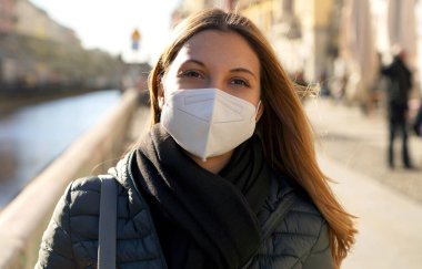Koruyucu maske takan umut dolu genç bir kadın rüzgarlı bir günde gün batımını seyrediyor.