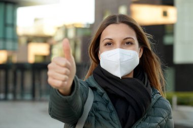 İyimser genç bir kız öğrencinin iyi niyet göstergesi. Hava kirliliği veya koronavirüs salgınından korunmak için koruyucu bir maske takıyor..
