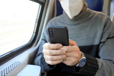 Toplu taşımacılıkta tıbbi maske takan bir adam. Zorunlu koruyucu maskeli, KN95 FFP2 cep telefonu taşıyan bir tren şoförü. Telefona odaklan..