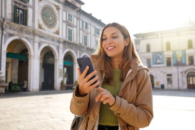 Avrupa 'nın eski kasabasında güneşli bir günde akıllı telefonuyla sohbet eden güzel bir kız.