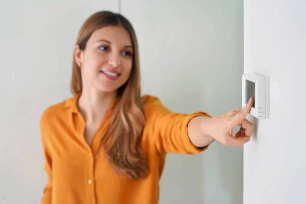 Lowering the temperature for energy saving. Young woman adjusting digital central heating thermostat at home. Focus on the hand.