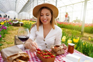 Güzel genç bir kadın piknik yapıyor. Kız çilek alır. Bahar zamanı kırsal kesimde taze hasat..