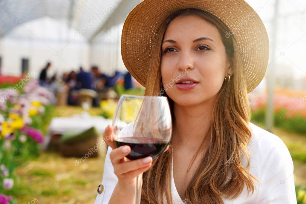 Image of cute young woman enjoying sitting outdors in park holding glass drinking wine