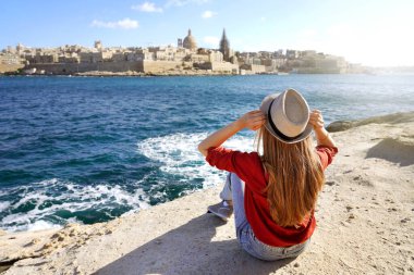 Young traveler woman holds hat looking at Valletta old town travel destination in Malta