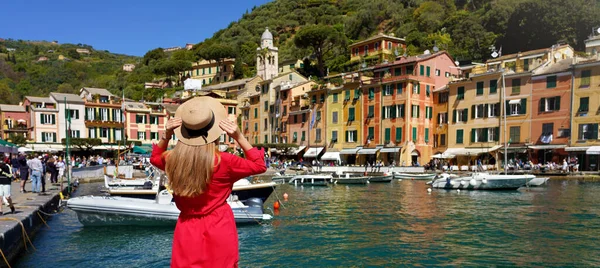 Portofino, İtalya 'da tatiller. Kırmızı elbiseli güzel bir kızın arka manzarası Portofino 'nun güzel köyünün keyfini çıkarıyor. Gemiler demirlemiş ve insanlar panoramik pankartıyla Piazzetta meydanında yürüyor..