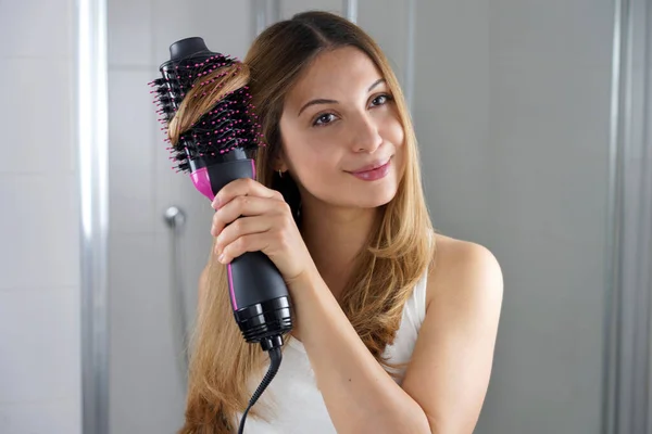 Girl using round brush hair dryer to style hair at the mirror in an easy way at home