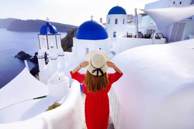 Santorini 'de tatil. Gezgin kadının arka manzarası geleneksel Oia köyünde mavi kubbeli kiliselerle ve Santorini Adası 'ndaki evlerle merdivenlerden iniyor..