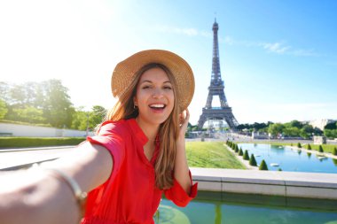 Kırmızı elbiseli ve şapkalı moda turisti Paris, Fransa 'da Eyfel Kulesi' nin arka planında kendi fotoğrafını çekiyor. Seyahat kavramı.