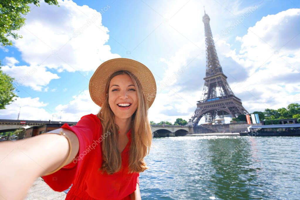 Young tourist woman making selfie photo with Eiffel tower on the background in sunny day in Paris, France