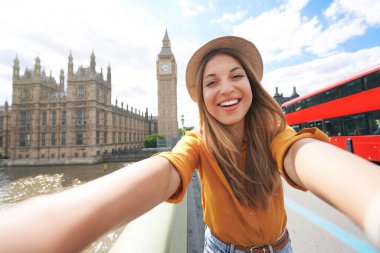 Gülümseyen turist kız Londra, İngiltere 'de kendi portresini çekiyor. Büyük Ben Kulesi, Westminster Sarayı ve güneşli yaz gününde çift katlı kırmızı otobüsle Londra 'da seyahat eden mutlu kadının selfie fotoğrafı..