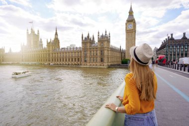 Tourism in London. Back view of traveler girl enjoying sight of Westminster palace and bridge on Thames with famous Big Ben tower in London, UK.