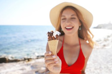 Bikinili kadın yazın plajda kameranın önünde dondurma külahı tutuyor. Dondurmaya odaklan..