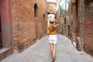 Toskana 'da tatil. İtalya 'nın Tuscany kentindeki Siena' nın dar sokakları arasında yürüyen güzel, şık turist kızın arka manzarası.