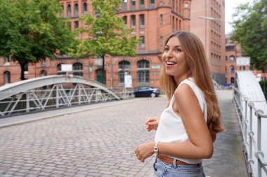 Çekici, pozitif kadın arkasını döner ve Kuzey Avrupa 'da bir şehir sokağına bakar.