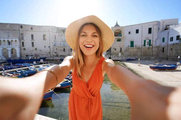 Selfie girl in southern Italy. Young tourist woman taking self portrait with the ancient port of Monopoli, Apulia, Italy.