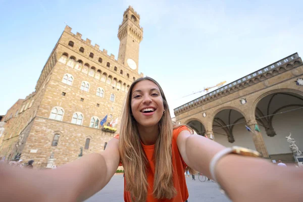 Self portrait of beautiful traveler woman smiling at camera in Piazza della Signoria square on sunset in Florence, Italy