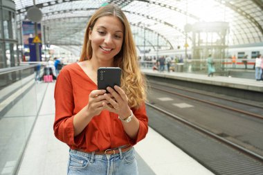 Gülümseyen çekici Brezilyalı yolcu tren istasyonunda akıllı telefonuyla internetten bilet alıyor. Boşluğu kopyala.