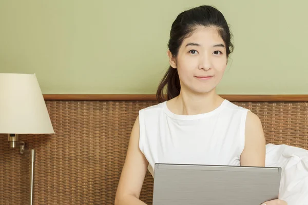 Gelukkig jonge Aziatische vrouw die werkt met laptop in slaapkamer — Stockfoto