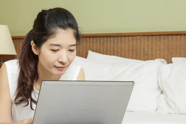 Feliz joven asiática mujer trabajando con portátil en dormitorio —  Fotos de Stock