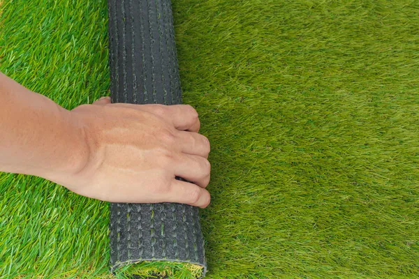 Kunstrasen grüne Rasenrolle mit der Hand lizenzfreie Stockfotos