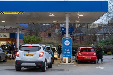 Wigan, İngiltere: 10 Mart 2022: İngiliz sürücüler panik içinde benzin alırken, Tesco benzin istasyonunda benzin almak için kuyrukta bekleyen arabalar