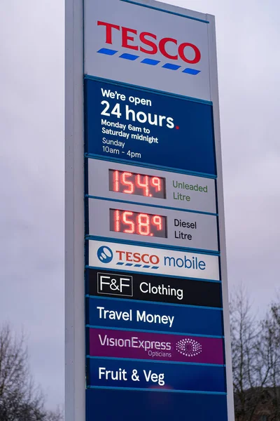 Wigan, İngiltere: 10 Mart 2022: Tesco süpermarket otoparkının girişindeki büyük ışıklı tabela şirket logosunu, açılış saatlerini ve litre benzin ve dizel fiyatını gösteriyor