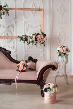 Sıcak bir odada, beyaz sıva ve bej perdelerin arka planında bir kanepe var, üzerinde bir sürü suni çiçek var.