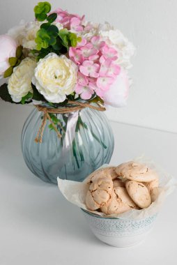 Beyaz bir masada çiçekli vazo. Masada kremalı bir tabak. Sabah kahvaltısı.