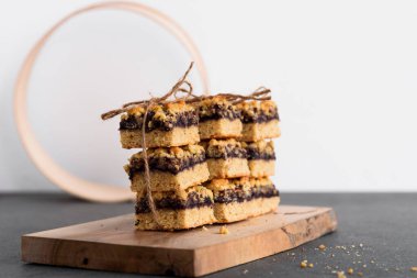 Pastanın reçelli parçaları istiflenmiş ve sicimle bağlanmış. Tahta bir tahtanın üzerinde. Gri bir masada. Arka planda ahşap elek.