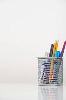 Beyaz arka planda, üzerinde kalem ve işaretler olan bir ağ camı var. Masanın üzerinde de ayna resmi var.