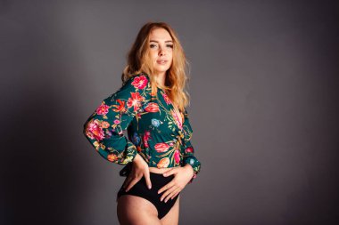 Genç sarışın bir kalça üzerine eğilmiş kameraya ve şaşılara bakıyor.