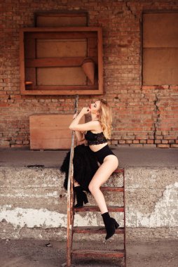 Sevimli bir kız tek kalçasının üstünde oturur. Sarışın bakışlarını kaçırıyor, dirseğini korkuluklara yaslıyor..