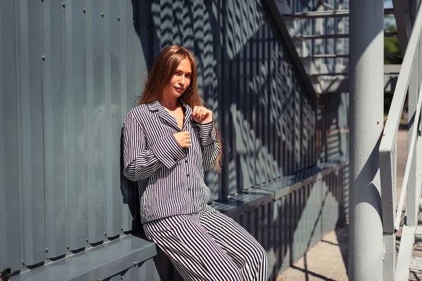 Çizgili siyah beyaz takım elbiseli kız demir bir binanın arka planında oturuyordu.